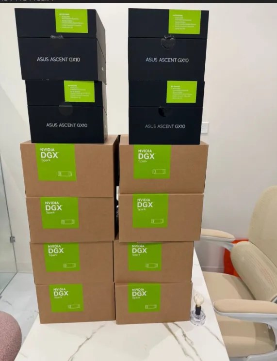 A photo of eight NVIDIA DGX Spark boxes and four ASUS Ascent GX10 boxes, stacked high in two rows on a table.