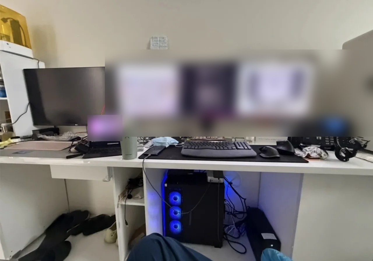 The director's desk. A widescreen monitor shows the clinic camera feed and a black command-line window. A laptop and an office phone sit beside it, and under the desk a computer with a blue light glows.