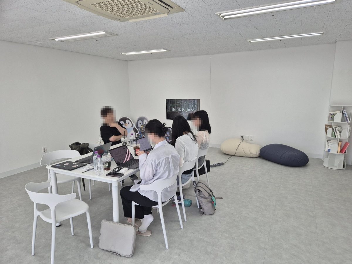 Participants sitting around a white table with laptops open, working and talking together. Faces are blurred