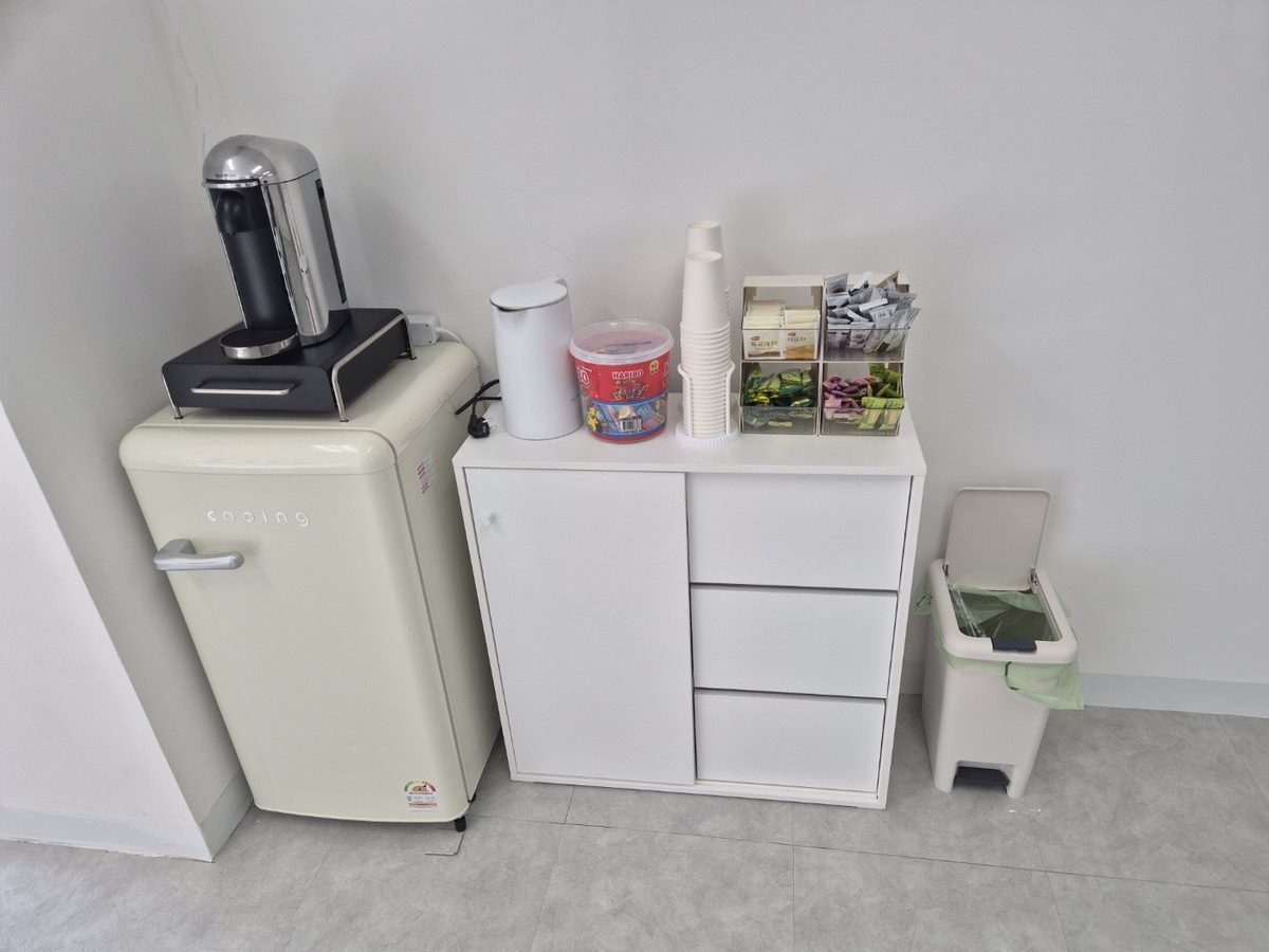 A snack corner in one part of the meeting space, with a refrigerator, coffee machine, paper cups, tea bags, and jelly candies