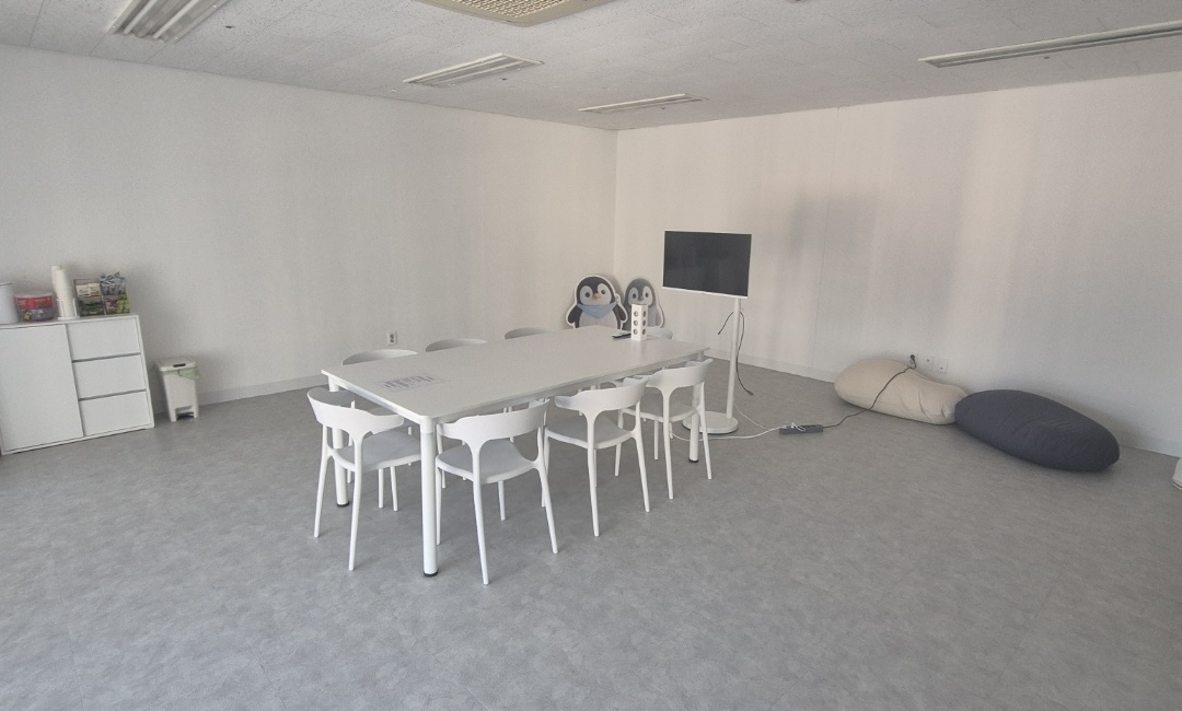 A spacious study area with white tables and chairs, monitors, a penguin standing sign, and a bean bag chair by the window